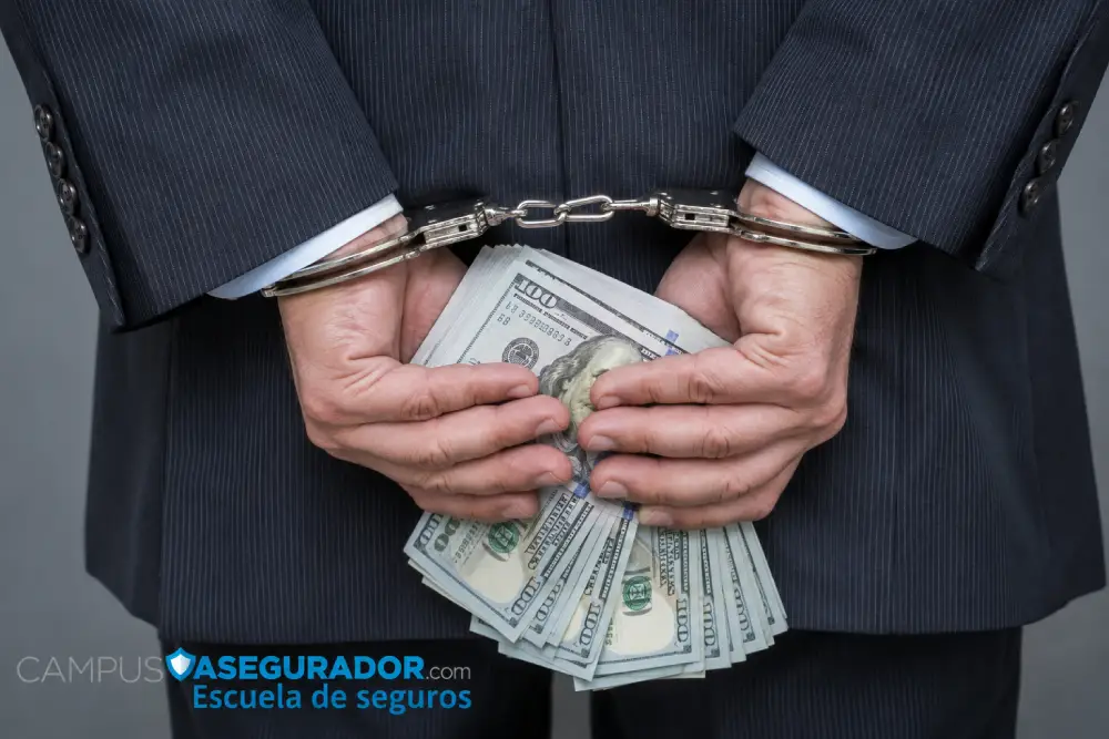 Hombre trajeado esposado sosteniendo billetes de cien dólares, ilustrando fraude financiero y delitos en seguros.